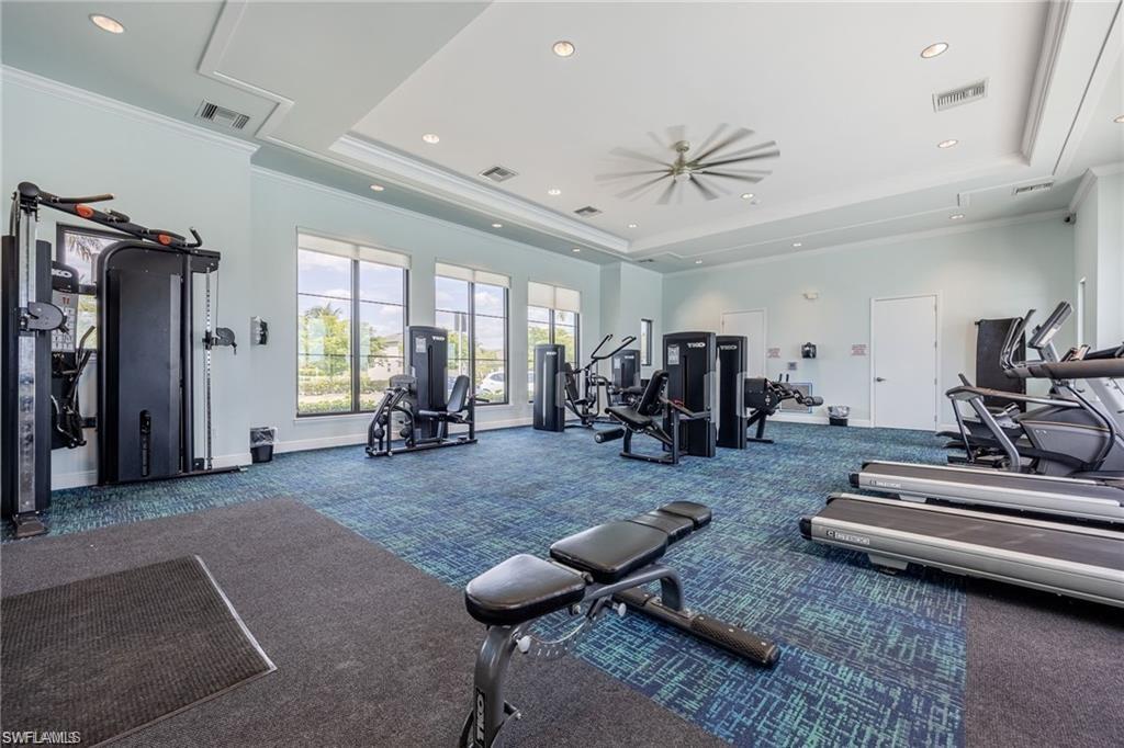 Spacious fitness room featuring a variety of exercise equipment, ample natural light from multiple windows, textured blue and gray carpet flooring, recessed lighting, and a contemporary ceiling fan