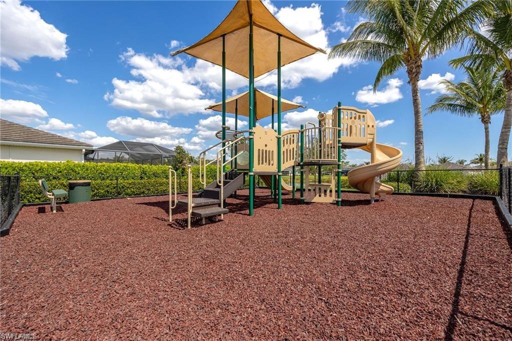 Community playground featuring a multi-level play structure with slides and climbing elements, shaded by overhead canopies