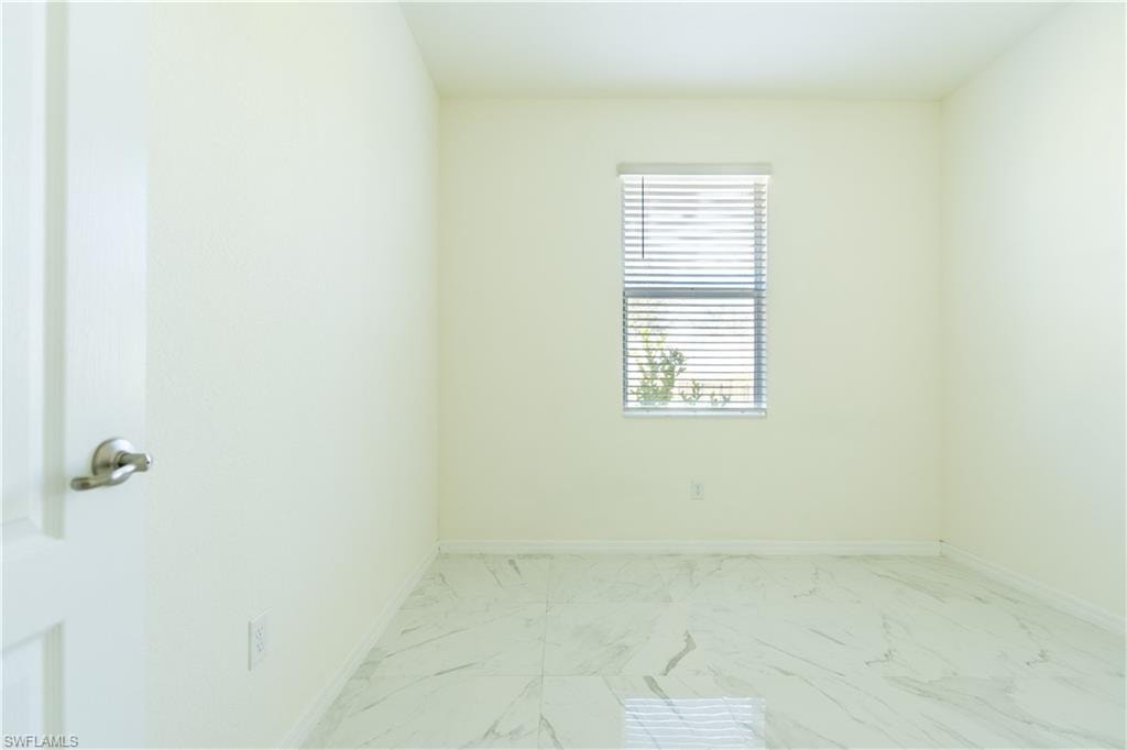 Bright room featuring white walls, a single window with horizontal blinds, and a white door with a brushed nickel handle