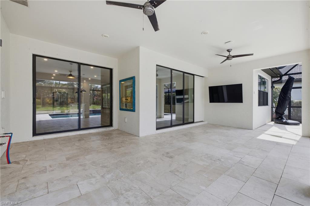 Spacious outdoor living area with light-toned rectangular tile flooring, multiple sliding glass doors, and two ceiling fans