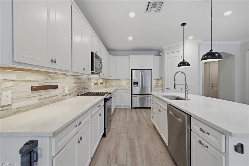 Modern kitchen featuring extensive white cabinetry, light-toned countertops, and a tiled backsplash