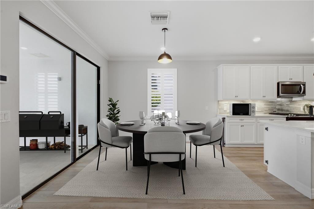 Open-concept dining area featuring wood-finish flooring, a contemporary pendant light fixture, and crown molding