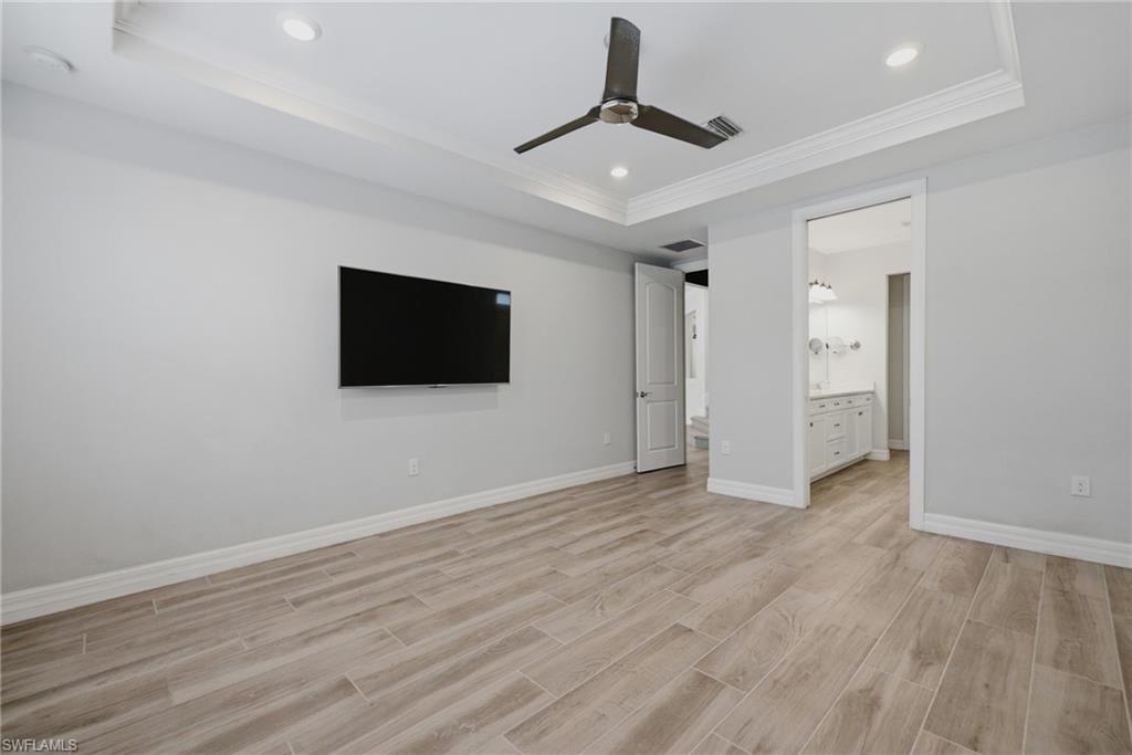 Spacious room featuring wood-finish flooring, a tray ceiling with recessed lighting, and a dark-toned ceiling fan