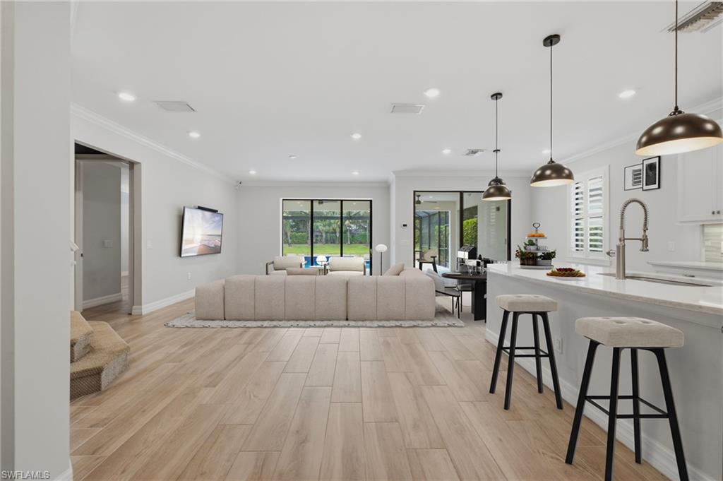 Open-concept living area featuring light wood-finish flooring, recessed lighting, and crown molding