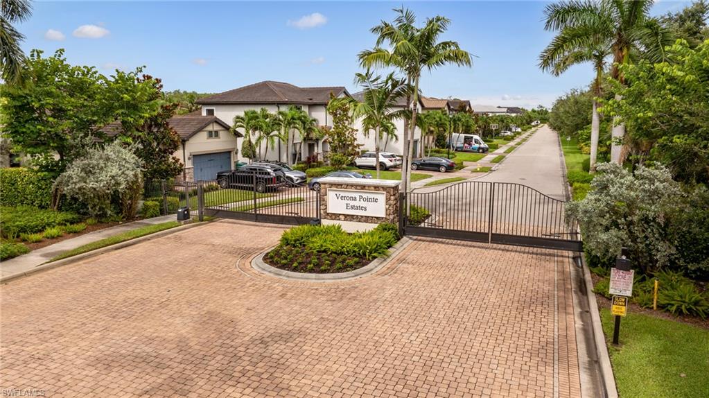 Gated community entrance featuring brick paver driveway and landscaping