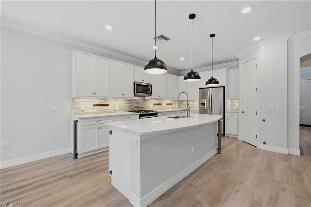 Modern kitchen featuring white cabinetry, a large kitchen island with integrated sink, stainless steel appliances, pendant lighting, and wood-finish flooring
