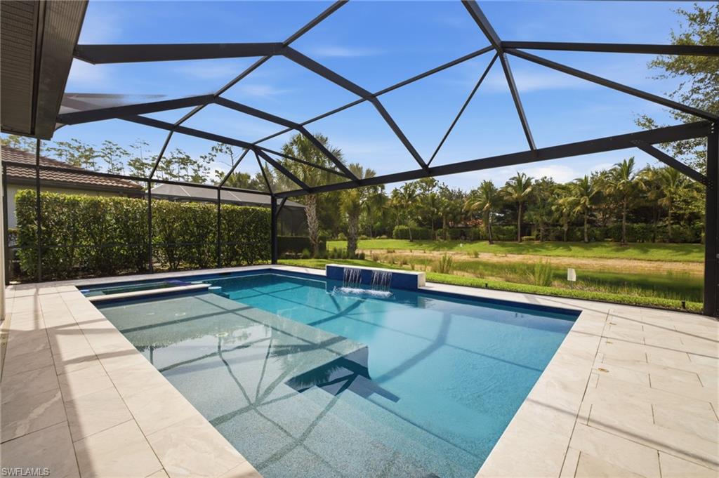 Screened pool enclosure featuring a rectangular pool with a waterfall element, integrated spa, and sun shelf
