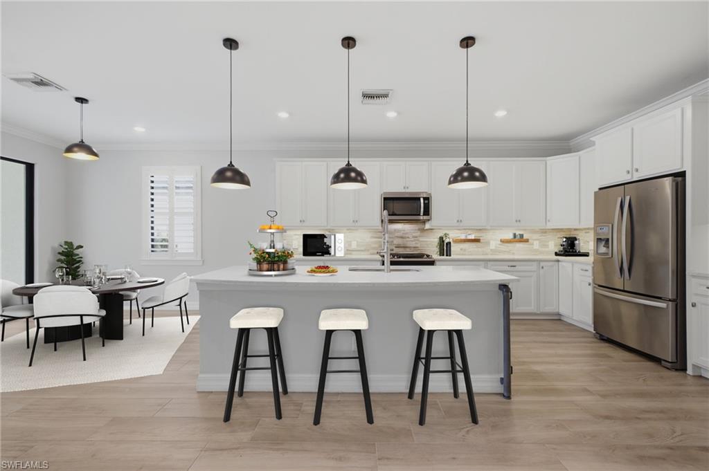 Modern kitchen featuring a large island with seating, stainless steel appliances, white cabinetry, wood-finish flooring, and pendant lighting