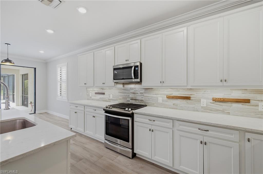 Modern kitchen featuring white shaker cabinetry, stainless steel appliances, light-toned countertops, a light-toned tile backsplash, and recessed lighting
