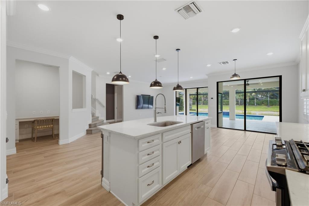 Modern kitchen featuring a white island with a stainless steel sink, coordinating pendant lighting, and wood-finish flooring
