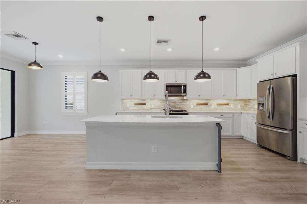 Kitchen featuring a large island with sink, white shaker cabinetry, stainless steel appliances, and wood-finish flooring