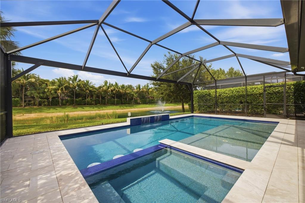 Screened pool enclosure featuring a multi-level pool with a waterfall feature, integrated spa, and light-toned paver decking