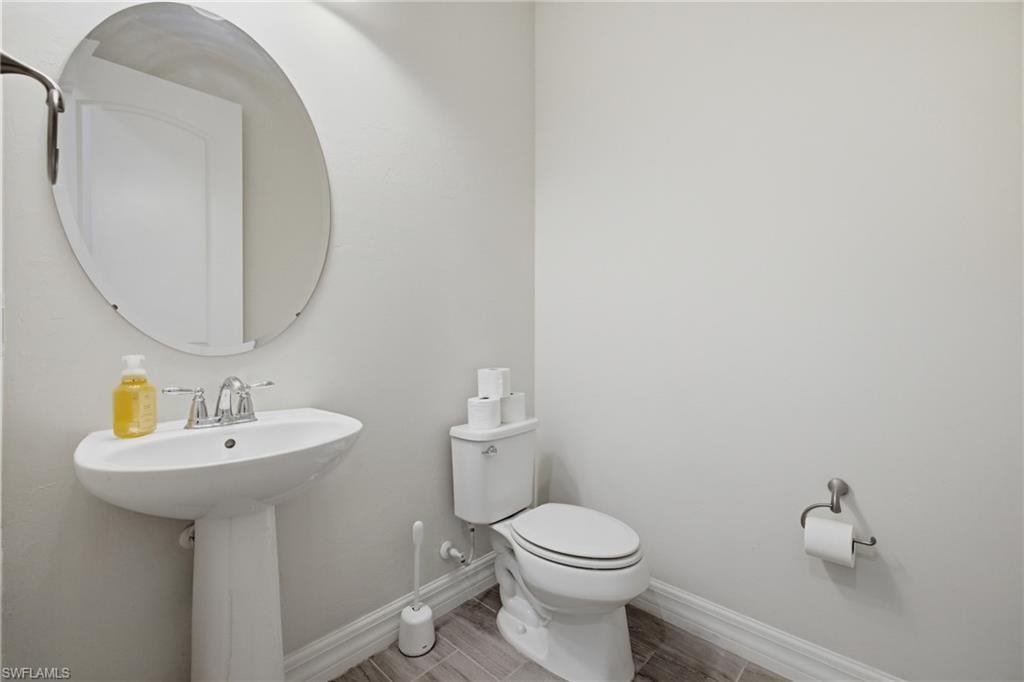 Pedestal sink with chrome faucet, oval mirror, and wood-finish tile flooring