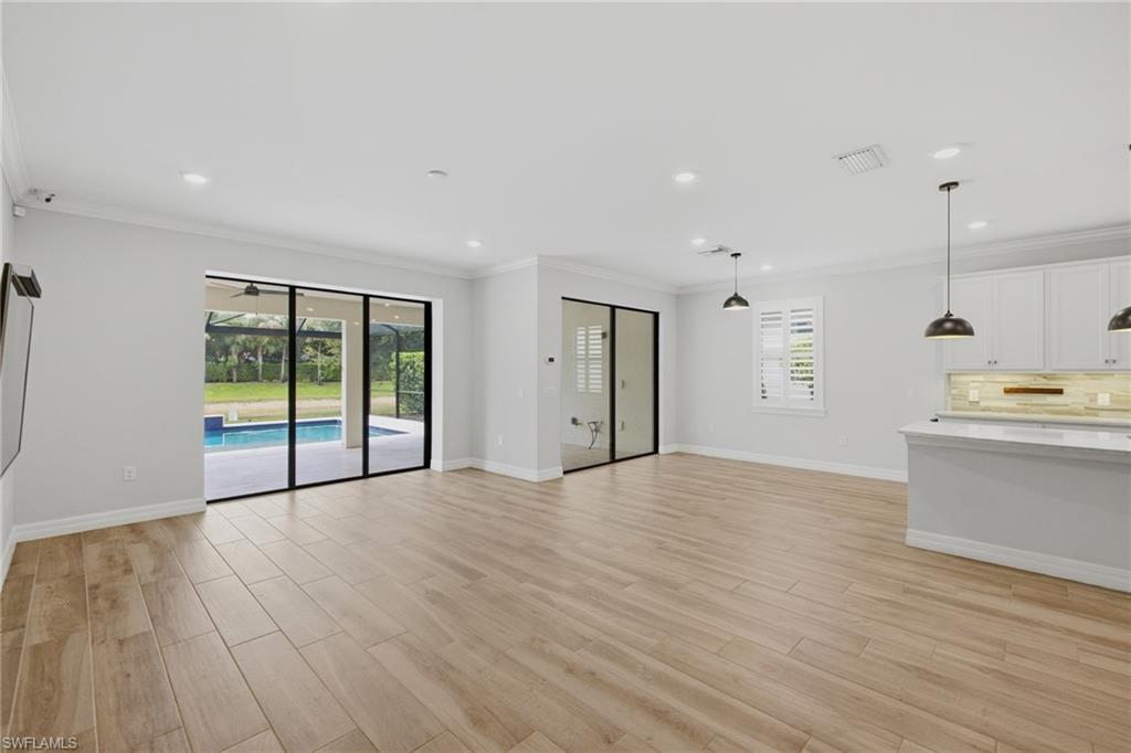Expansive main living area featuring wood-finish flooring, a kitchen island with stone countertop, white shaker cabinetry, recessed lighting, and sliding glass doors opening to a screened patio with a pool