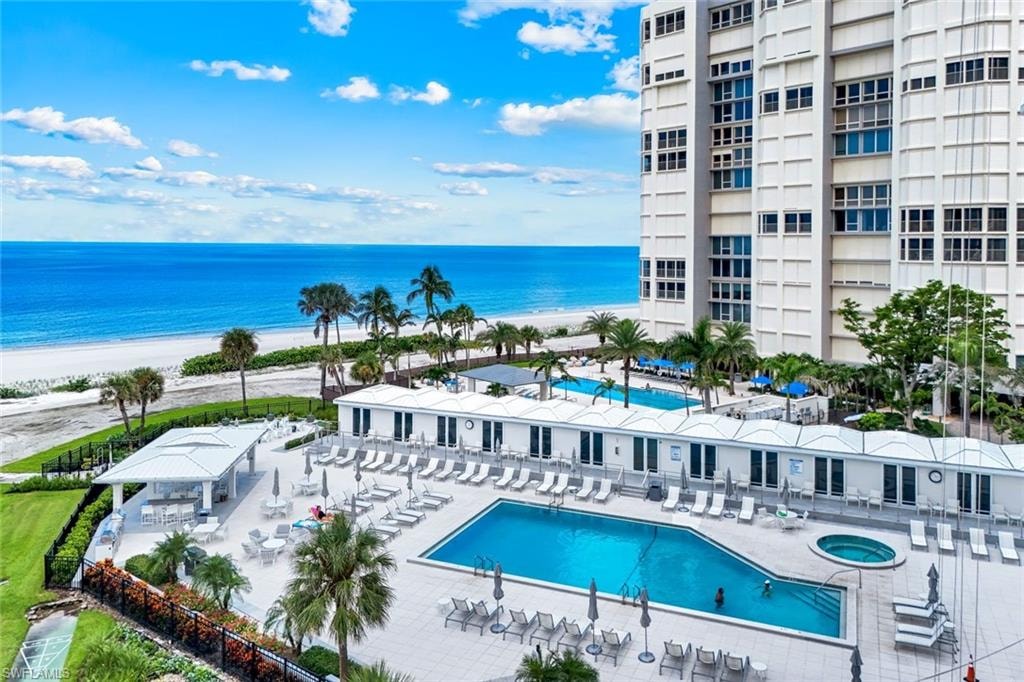 Community pool with a hot tub, view of water and beach, and a patio area