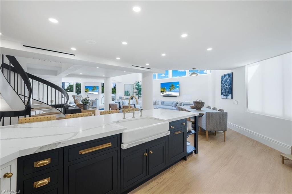 Kitchen with light stone countertops, recessed lighting, light wood-style floors, open floor plan, and dark cabinets