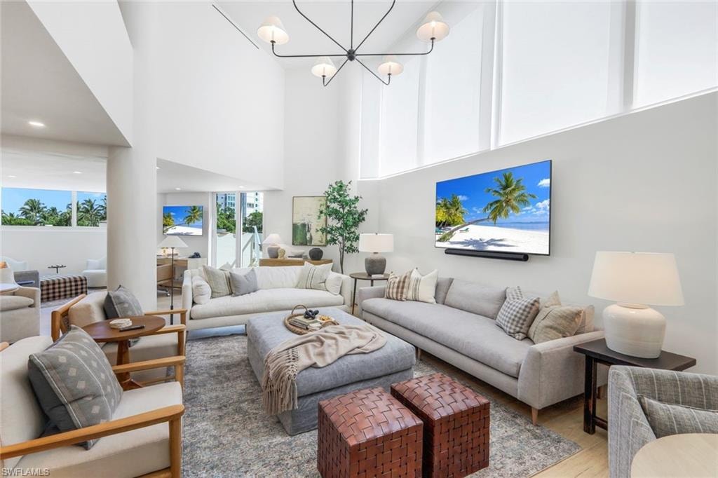 Living room with wood finished floors, a towering ceiling, a chandelier, and recessed lighting