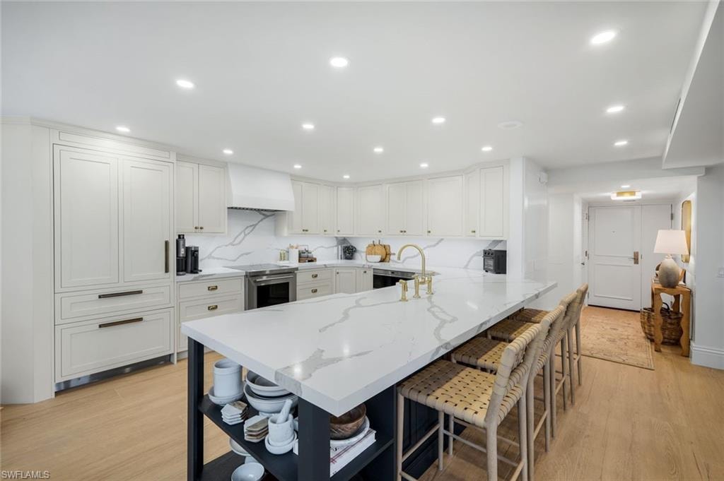 Kitchen featuring white cabinets, a peninsula, light stone counters, a breakfast bar area, and decorative backsplash