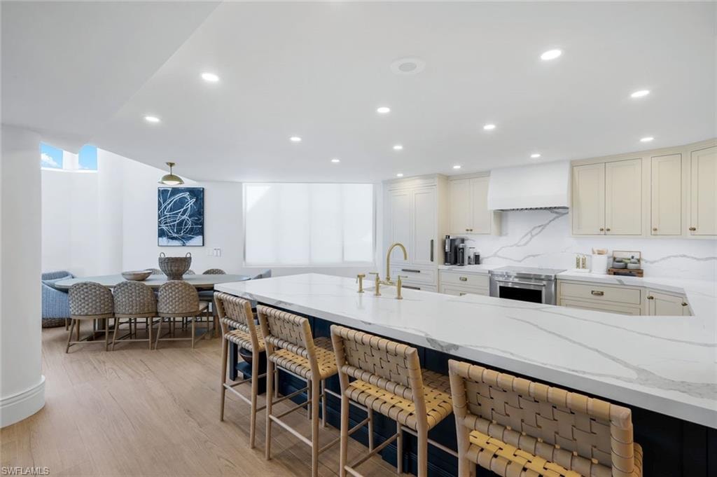 Kitchen featuring light stone counters, custom exhaust hood, recessed lighting, decorative backsplash, and a kitchen breakfast bar