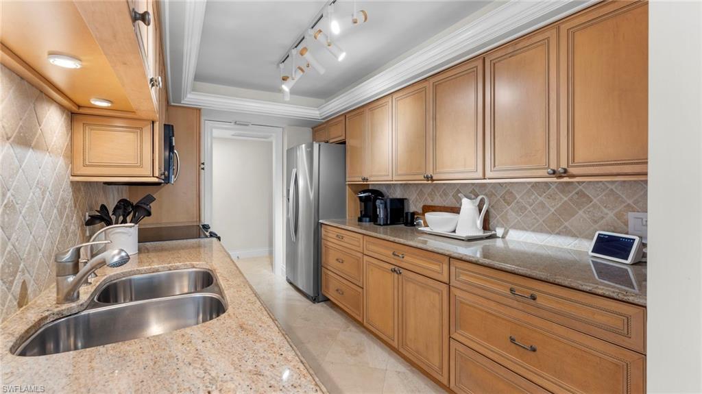 Kitchen featuring sink, decorative backsplash, a raised ceiling, appliances with stainless steel finishes, and light stone countertops