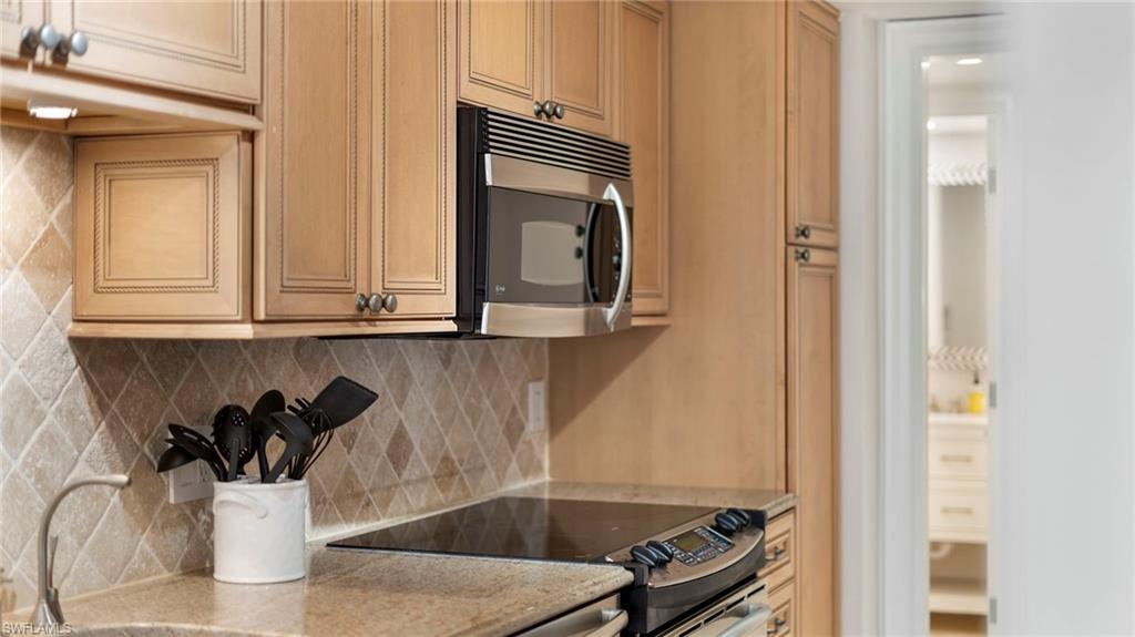 Kitchen featuring light stone countertops, black range oven, backsplash, and light brown cabinets