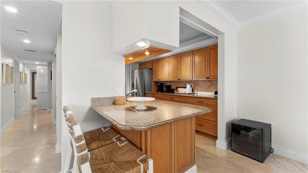 Kitchen featuring ornamental molding, kitchen peninsula, tasteful backsplash, stainless steel refrigerator with ice dispenser, and a kitchen bar
