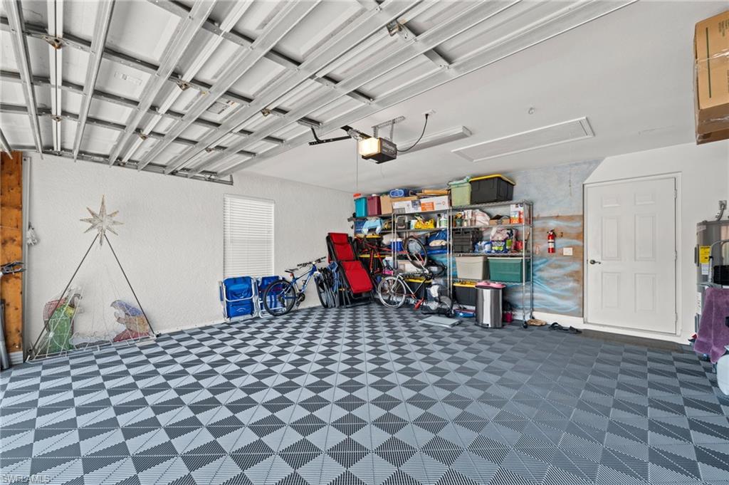 Spacious garage featuring checkerboard-patterned flooring, exposed ceiling beams, white textured walls, a single window with horizontal blinds, and a white paneled entry door