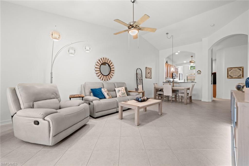 Spacious living area featuring light tile flooring, vaulted ceilings, and an arched entryway