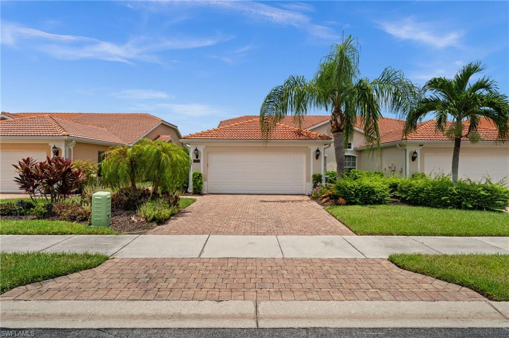 Mediterranean-style exterior featuring a terracotta tile roof, dual garage doors, and a paver driveway