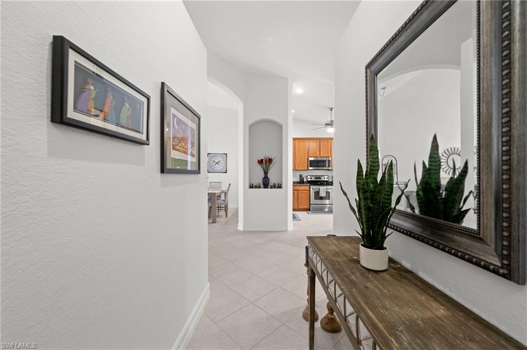 Hallway featuring light-toned tile flooring, white baseboards, and arched doorways