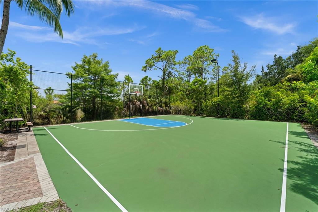 Outdoor basketball court featuring a green playing surface with blue key, clear backboard, and perimeter fencing