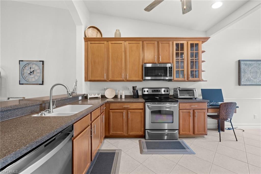 Kitchen featuring wood-finish cabinetry, stainless steel appliances, a built-in desk area, and a vaulted ceiling