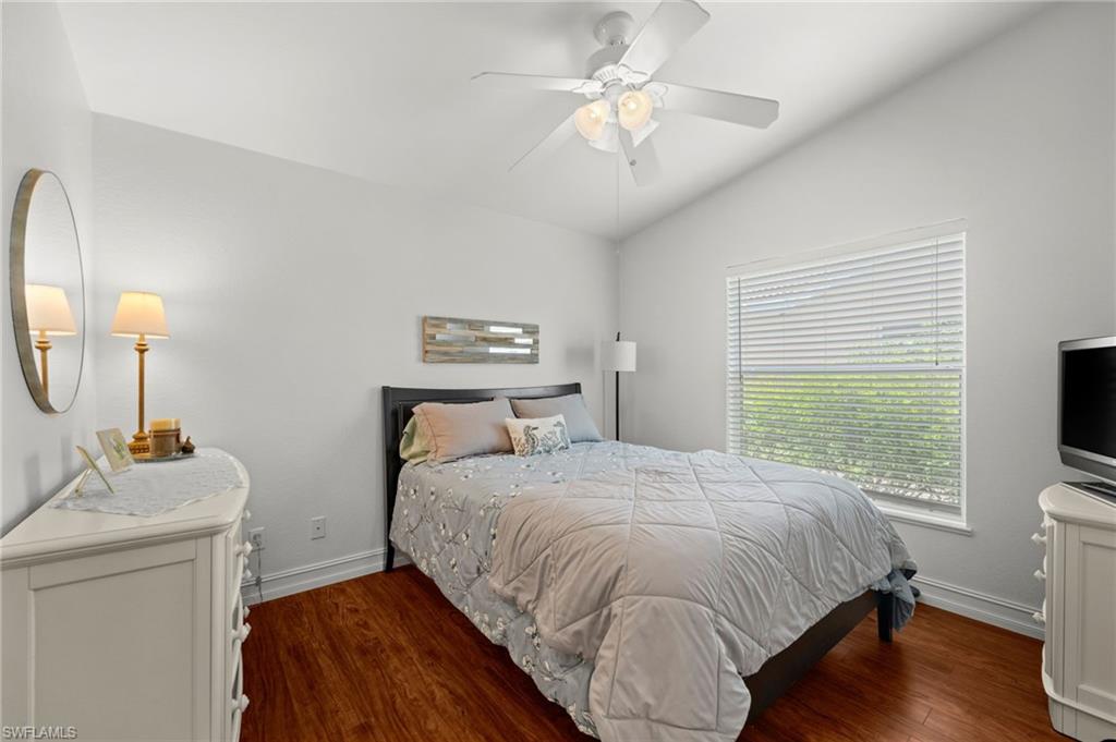 Bright room featuring a vaulted ceiling with a ceiling fan, wood-finish flooring, and a large window with blinds