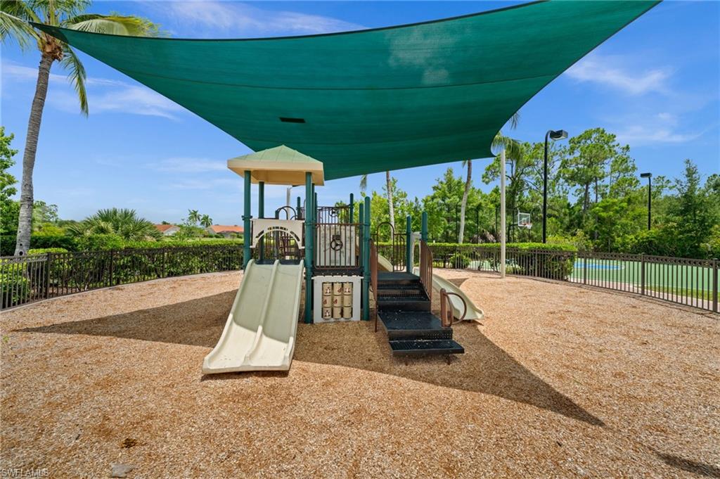 Playground area featuring a multi-level structure with slides and climbing elements, covered by a large green shade canopy
