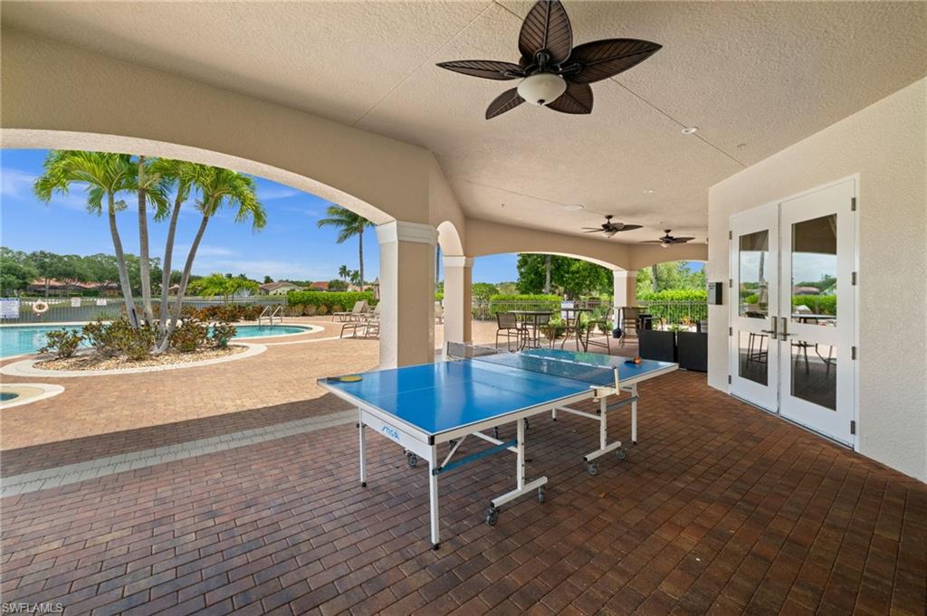 Covered outdoor patio featuring a brick-patterened paver floor, multiple ceiling fans, and arched openings