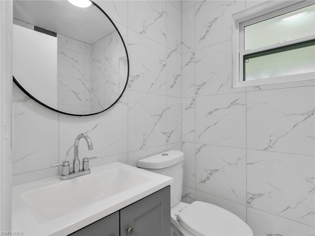 Bathroom featuring full-height white tile walls with gray veining, a white vanity with gray cabinetry, and a chrome faucet