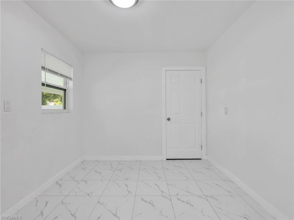 Bright interior space featuring white walls, a single window, a paneled door, and large format marble-look tile flooring
