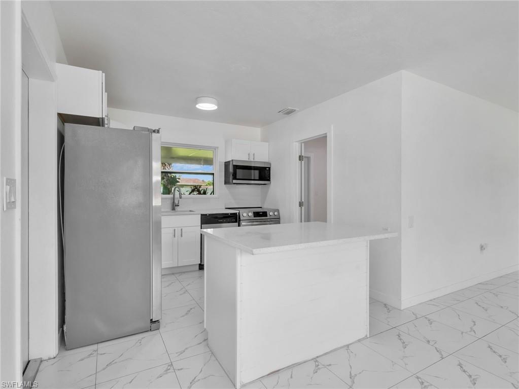 Modern kitchen featuring white cabinetry, stainless steel appliances, a white quartz countertop island, and white tile flooring