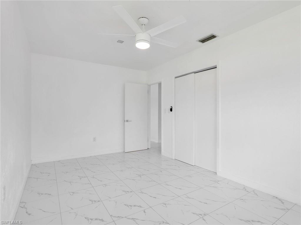Spacious room featuring white walls, large format tile flooring, a ceiling fan with integrated lighting, and a closet with bifold doors