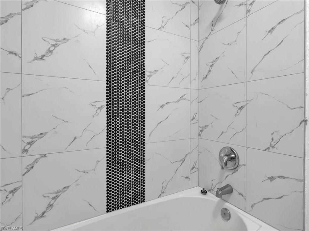 Bathtub and shower combination featuring white large-format wall tiles with grey veining, a black hexagonal mosaic accent strip, and chrome fixtures
