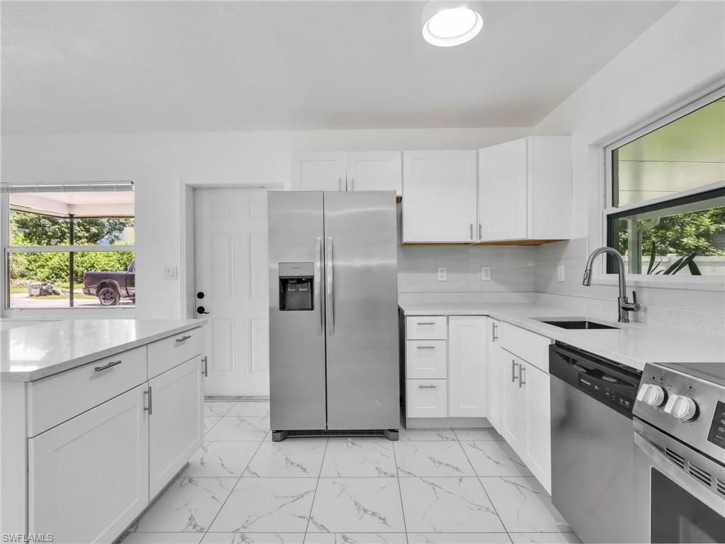 Modern kitchen featuring white shaker cabinetry, stainless steel appliances, marble-look tile flooring, light-toned countertops, and a single basin sink with a gooseneck faucet