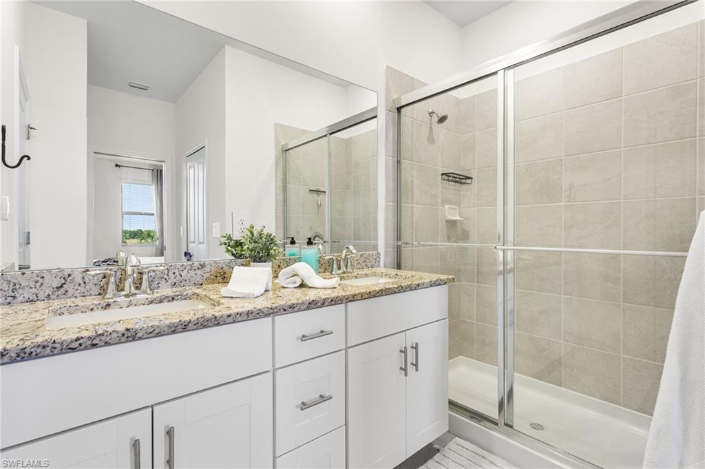Spacious primary bathroom featuring a dual-sink granite vanity, glass-enclosed walk-in shower, and private water closet