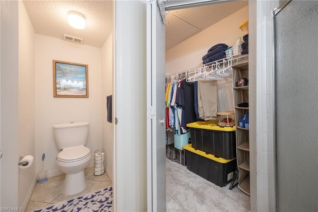 Powder room featuring tile flooring and an overhead light fixture, located beside a walk-in closet with carpet flooring and built-in wire shelving