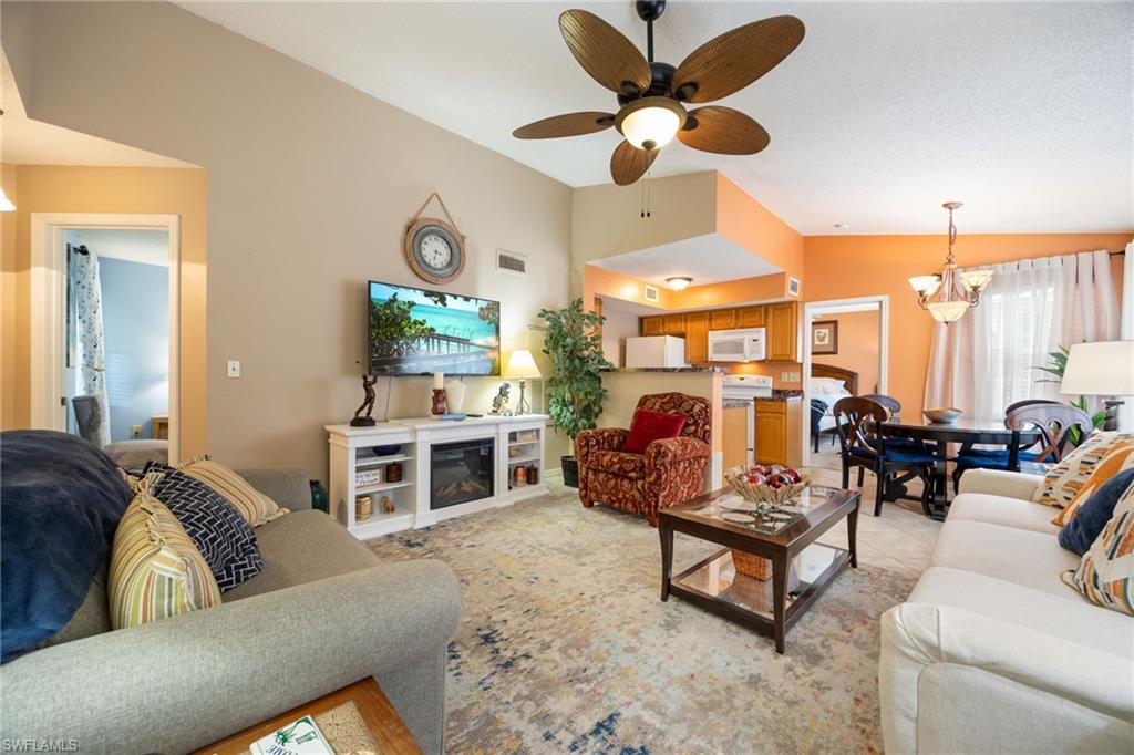 Open-concept living area featuring a vaulted ceiling with a ceiling fan, a built-in media console with an electric fireplace, and a dining area with a chandelier