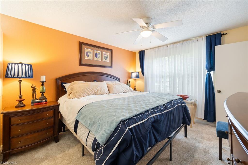 Carpeted bedroom featuring a ceiling fan, wall-to-wall window with blinds and curtain rods, and a solid door
