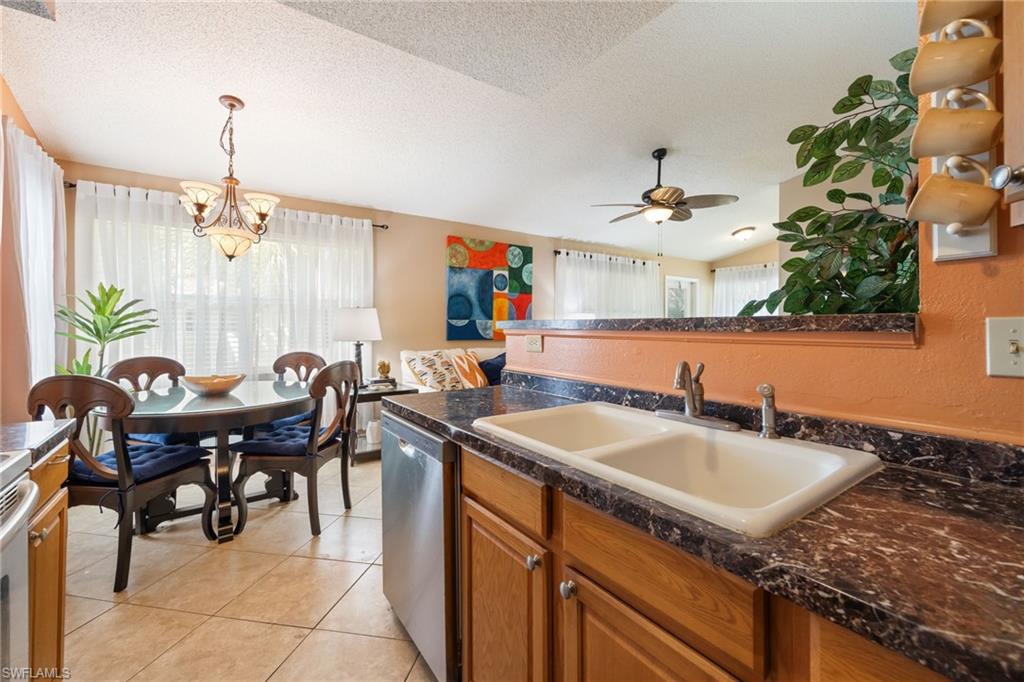 Kitchen featuring a dual-basin sink, dark speckled countertops, wood-finish cabinetry, and a dishwasher