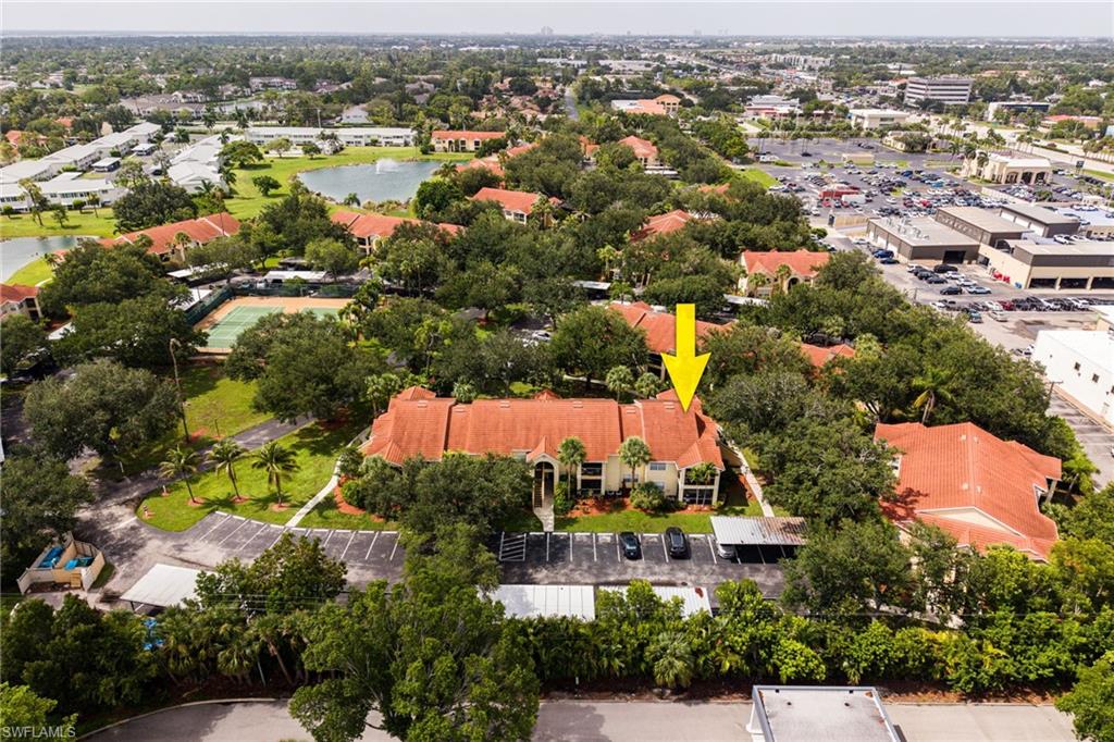 Aerial perspective highlighting a multi-building complex featuring red tile roofs, numerous mature trees, and a central parking area with covered spaces