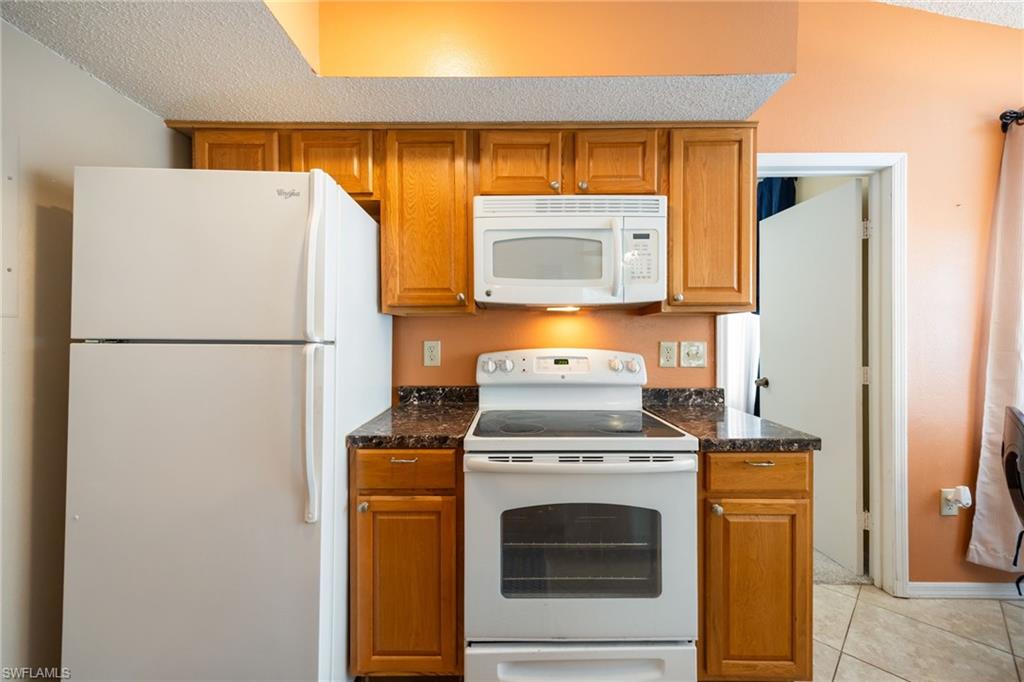 Kitchen featuring wood cabinetry, dark speckled countertops, and white appliances including a refrigerator, electric range, and microwave