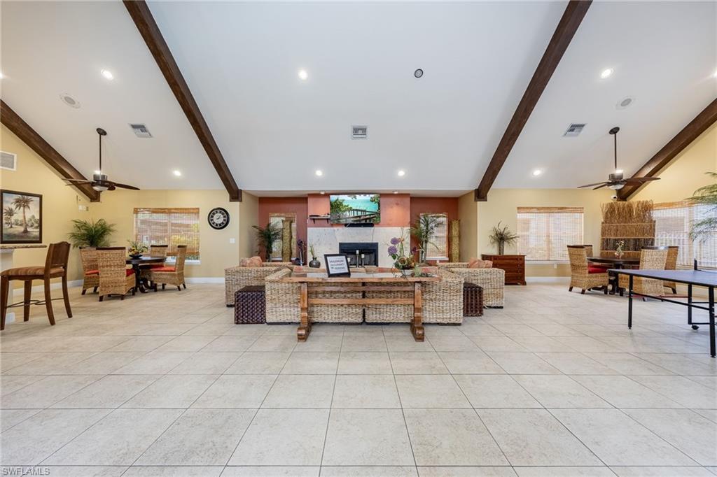Spacious room featuring vaulted ceilings with exposed wood beams, recessed lighting, ceiling fans, and large format tile flooring