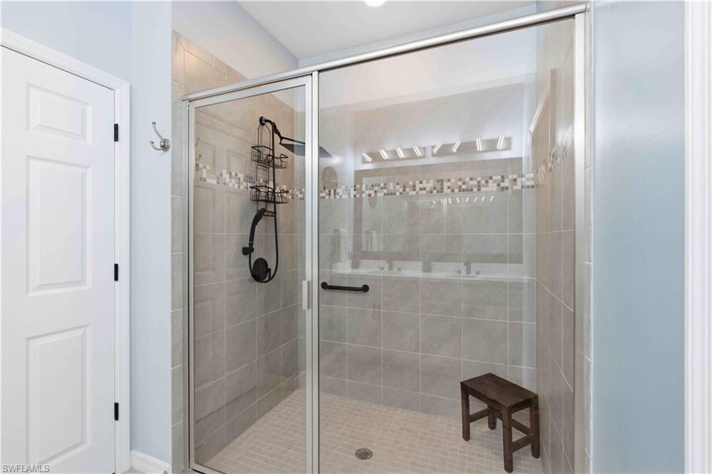 Glass-enclosed shower featuring large format wall tiles, a decorative mosaic tile band, and a textured floor